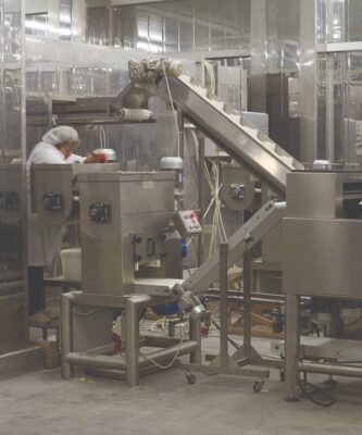 Two incline conveyor belts are moving product through a factory while a worker tends to the machine.